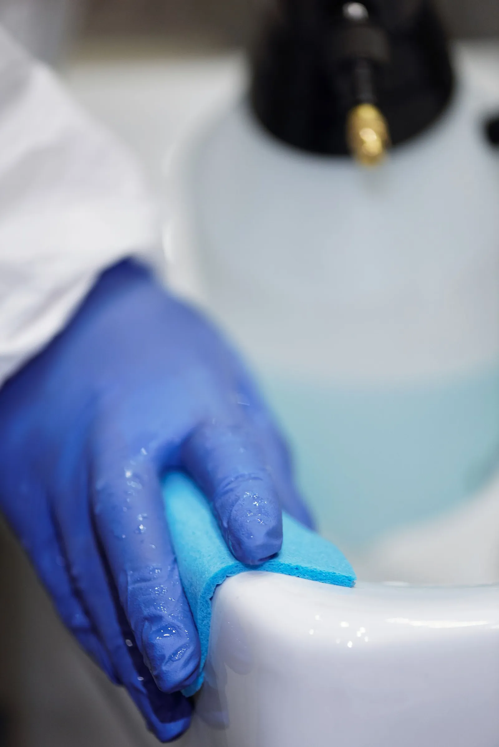 Gloved hands carefully cleaning a bathroom sink